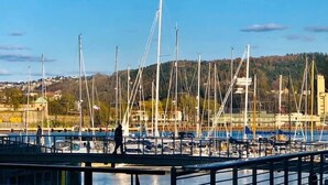 Un puerto deportivo con varios veleros amarrados, un puente peatonal y un paisaje montañoso al fondo.