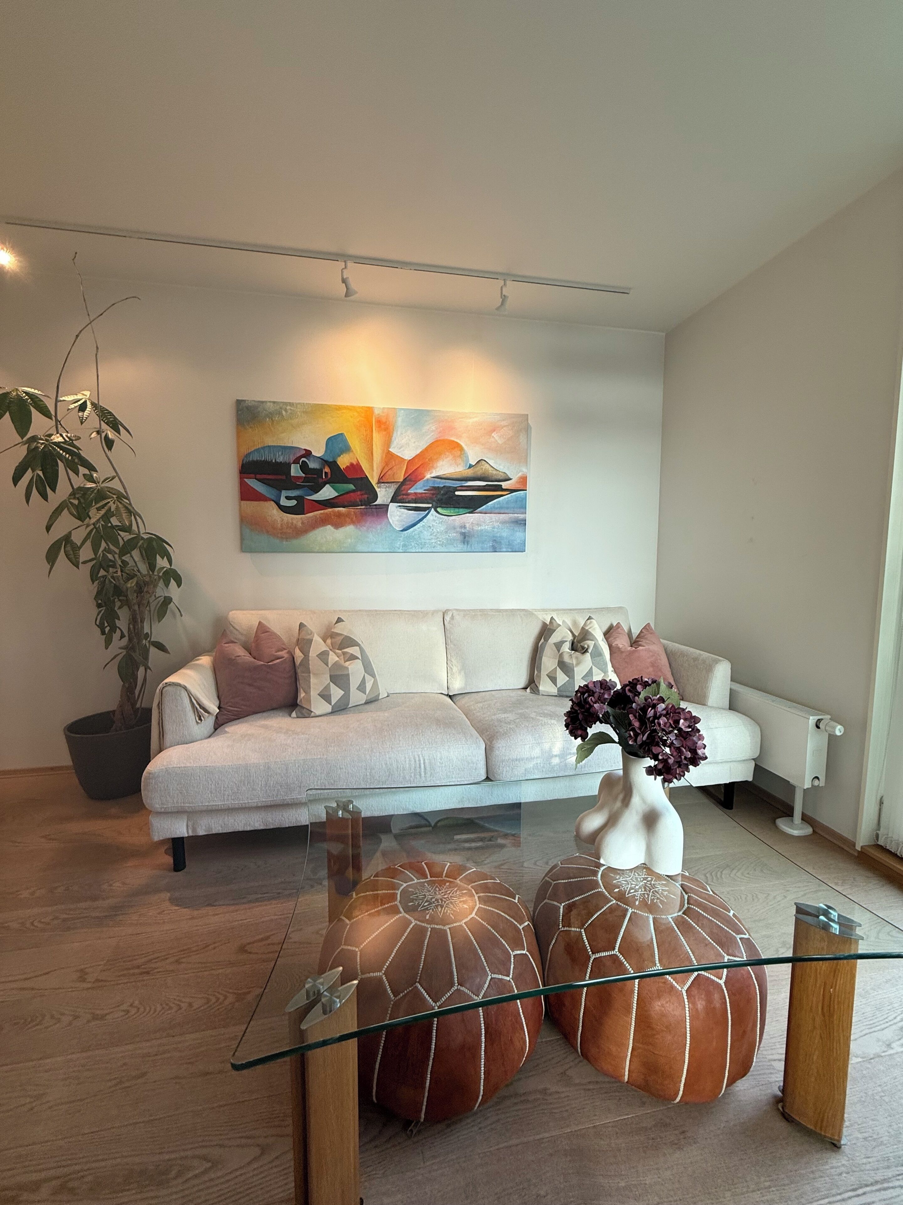 A modern living room with a sofa, a coffee table with decorative items, a potted plant, and a painting on the wall.