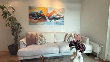 A modern living room with a sofa, a coffee table with decorative items, a potted plant, and a painting on the wall.