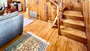 A wooden interior with a staircase, a sofa, and a patterned rug.