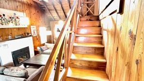 A wooden staircase leading to an upper level, a fireplace, and a sofa in a cabin-style interior.