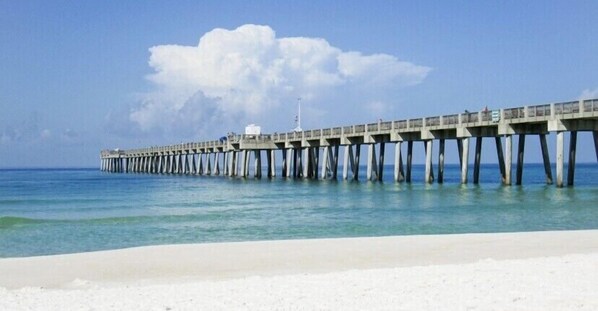 A pier extending into the ocean with a clear sky and a sandy beach in the foreground.