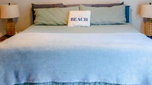 Un dormitorio con cama, ventilador de techo, cuadro colgado en la pared y dos lámparas de noche.