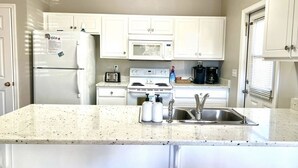 Una cocina con armarios blancos, un refrigerador, un microondas, una estufa y un lavamanos.