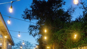 Un patio trasero con valla de madera, dos sillas Adirondack y una guirnalda de luces.