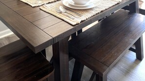 Una mesa de comedor dispuesta con platos, cuencos y cubiertos blancos, acompañada de un cactus y una copa de vino, con una ventana al fondo.