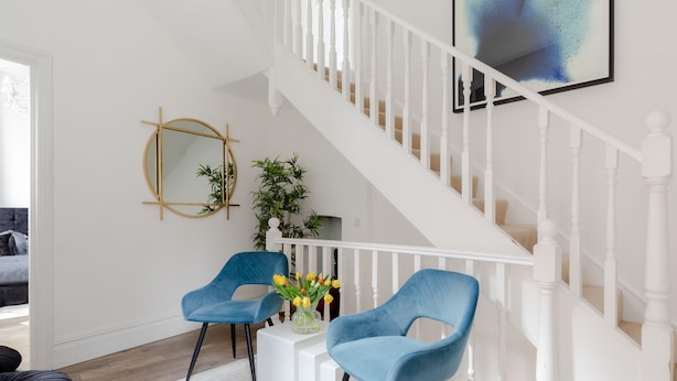 A modern living room with two blue chairs, a white coffee table, a staircase with white railings, and a framed abstract painting on the wall. - Refurbished! OXFORD STREET PHENOMENAL XXL DESIGN HOUSE IDEAL FOR GROUPS (London)