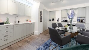A modern kitchen with white cabinets, a dining area with a glass table and chairs, and a blue rug. - Refurbished! OXFORD STREET PHENOMENAL XXL DESIGN HOUSE IDEAL FOR GROUPS (London)