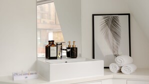 A bathroom with a white sink, a framed palm leaf artwork, and neatly rolled towels. - Refurbished! OXFORD STREET PHENOMENAL XXL DESIGN HOUSE IDEAL FOR GROUPS (London)