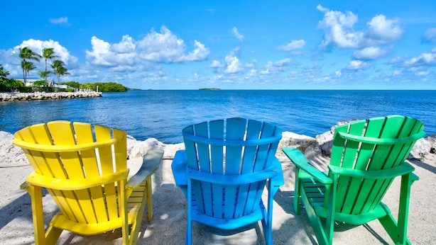 Tre poltrone Adirondack rivolte verso una spiaggia con vista libera sull'oceano e un'isola in lontananza.