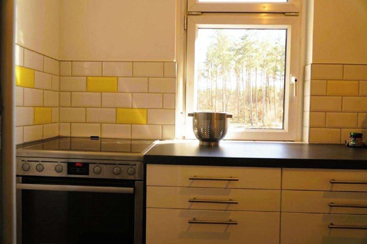 Une cuisine avec des carreaux blancs et jaunes, une cuisinière, un four et une fenêtre donnant sur des arbres.