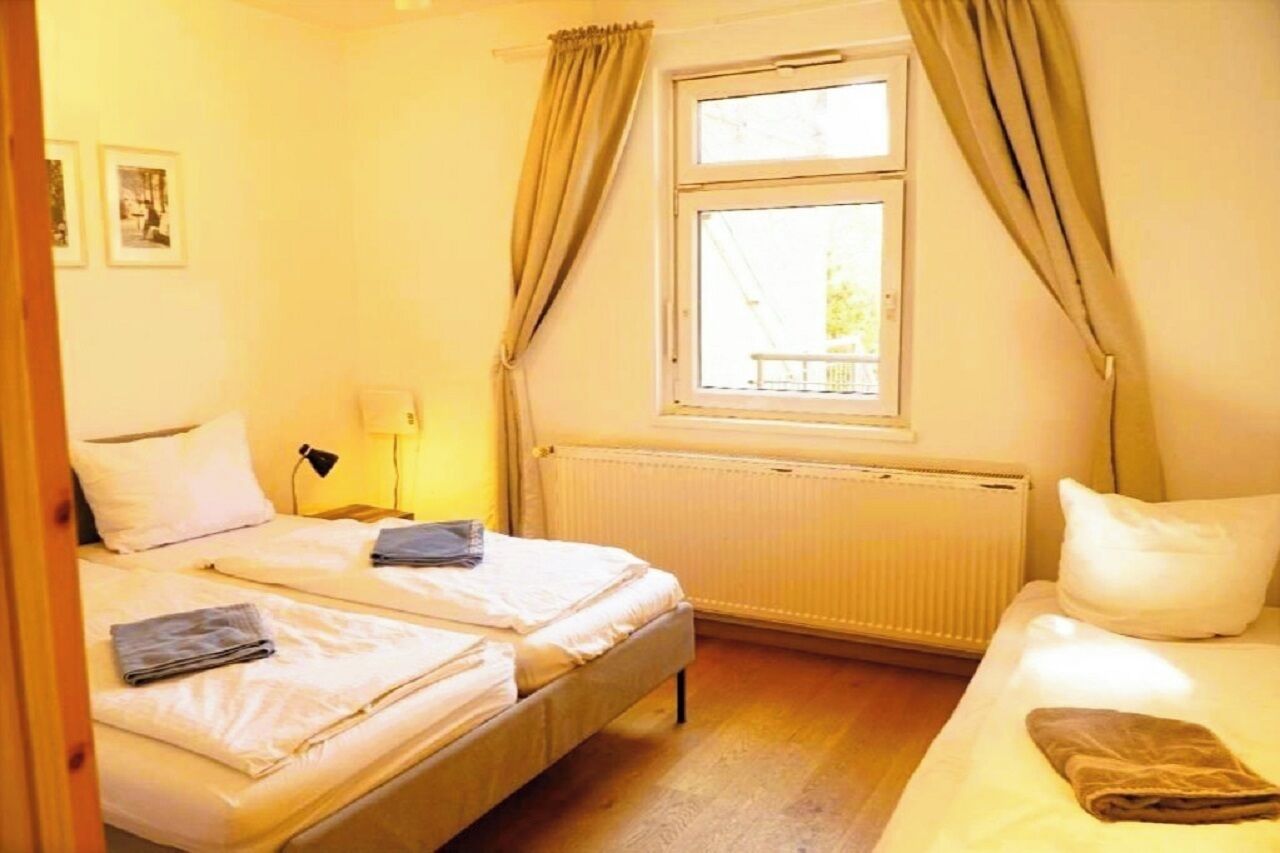 A room with two beds, a window with curtains, a radiator, and a lamp.