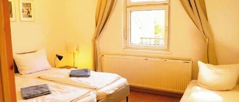 A room with two beds, a window with curtains, a radiator, and a lamp.