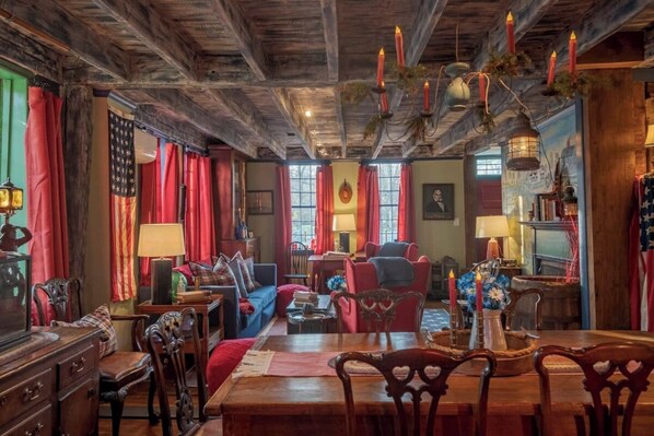 A traditional room with a wooden ceiling, red curtains, a dining table, and a blue sofa.