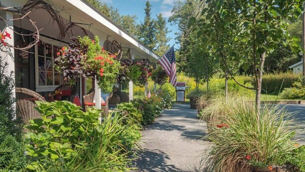 A pathway leading to a building with an American flag, surrounded by lush greenery and potted plants.