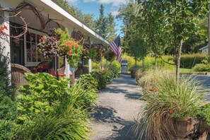 Un chemin menant à un bâtiment orné d’un drapeau américain, entouré d’une végétation luxuriante et de plantes en pot.