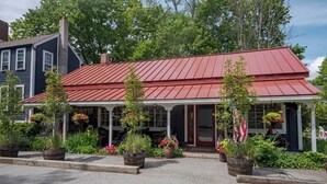 A two-story building with a red metal roof and a porch with potted plants.