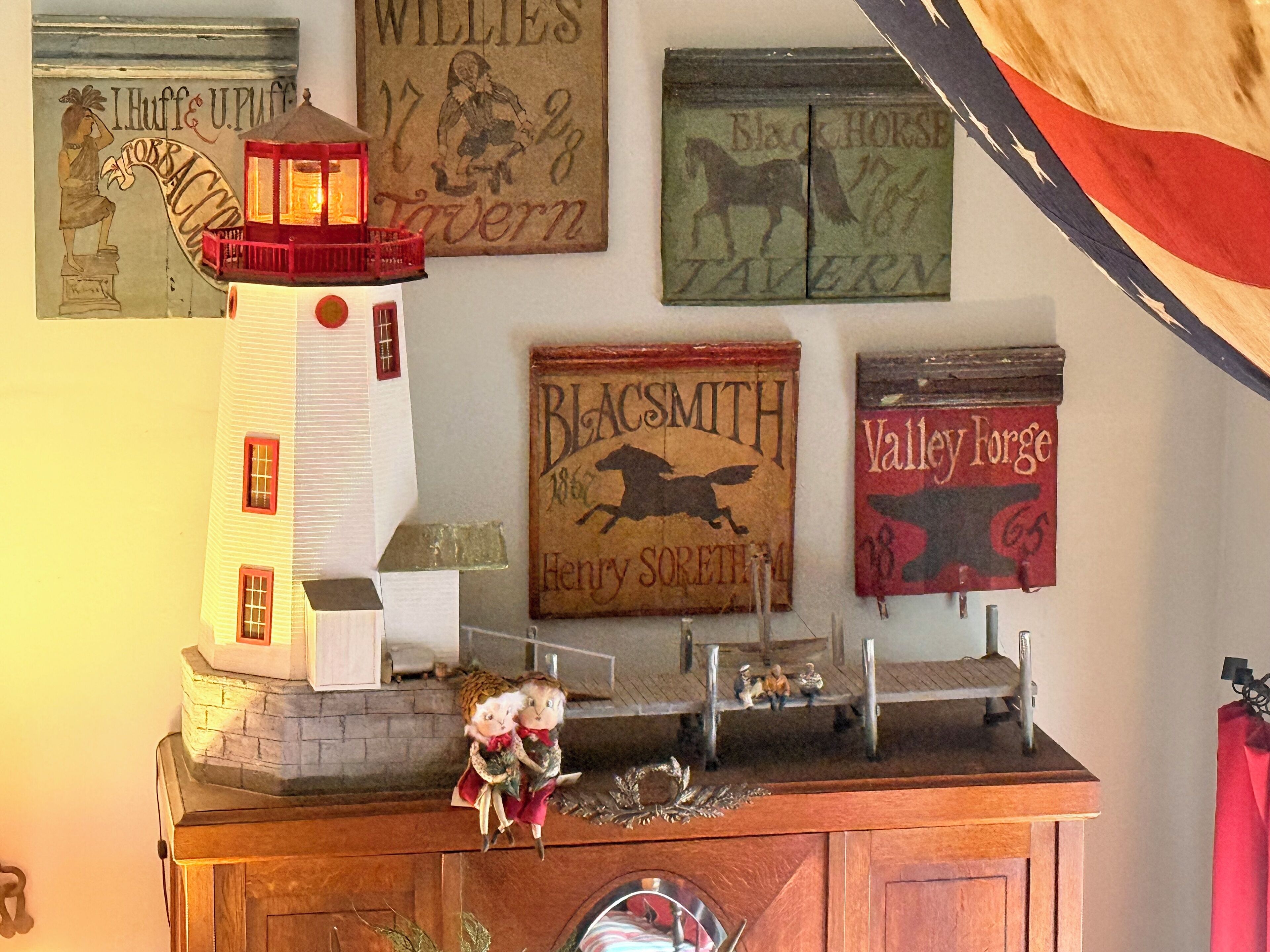 A collection of vintage signs and a model lighthouse on a mantelpiece.