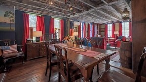 A room with a wooden dining table, chairs, a flag, and red curtains. - Historic 1807 Williams Home... A Nautical New England Inspiration!  (Old Mystic)