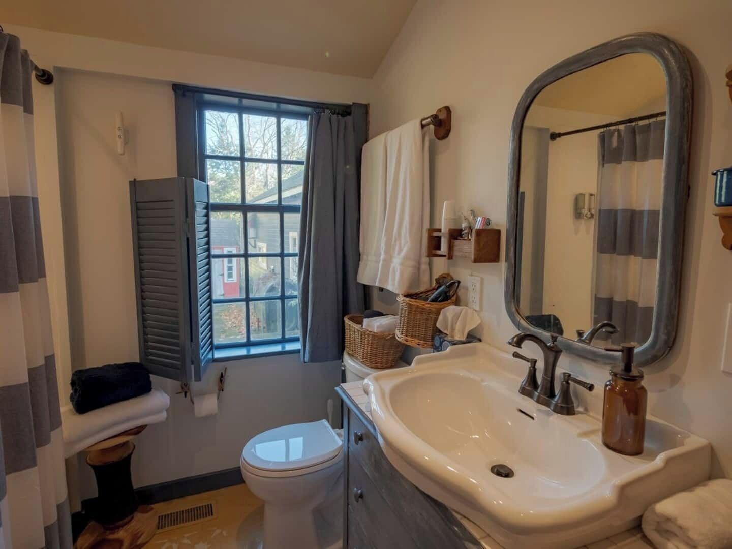 Un baño con lavamanos blanco, un espejo, un inodoro y una ventana con cortinas.