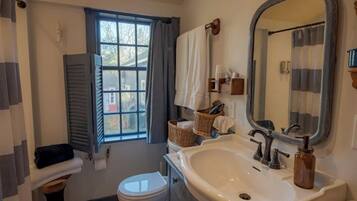 Un baño con lavamanos blanco, un espejo, un inodoro y una ventana con cortinas.