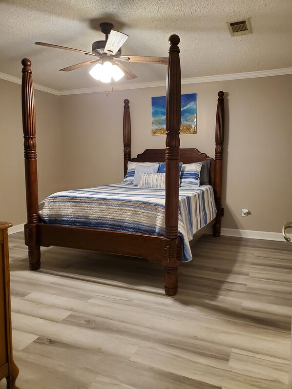 A four-poster bed with a wooden frame and a ceiling fan above. - Peggy Sue (Pass Christian)