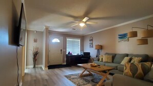 A living room with a ceiling fan, a television mounted on the wall, a sofa, a coffee table, and a patterned rug. - Peggy  Sue (Pass Christian)