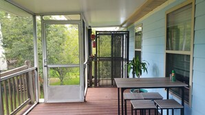 A covered porch with a wooden deck, a table with chairs, and a potted plant. - Peggy  Sue (Pass Christian)