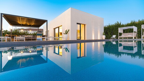 Uma área de piscina moderna com piscina transparente, espreguiçadeiras e um espaço de estar coberto.
