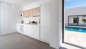 Cozinha moderna com armários brancos, micro-ondas embutido e vista para uma piscina através de uma porta de vidro.