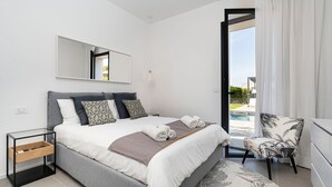 Quarto moderno com cama, mesa de cabeceira, cadeira e vista para o exterior.
