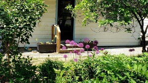 Una casa con porche, rodeada de abundante vegetación y plantas florecientes.