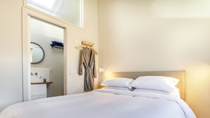 Una cama bien hecha con sábanas blancas, cabecera de madera y una lámpara de noche.