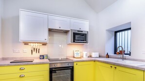 Una cocina moderna con armarios superiores blancos, un mueble inferior amarillo, horno empotrado, microondas y una ventana con persianas.