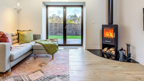 Una sala de estar con sofá, alfombra estampada, chimenea y puerta corrediza de vidrio que da a un patio trasero.