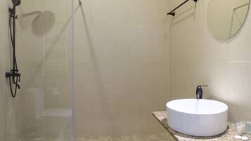 A bathroom with a glass-enclosed shower, a round sink, and a mirror on the wall.
