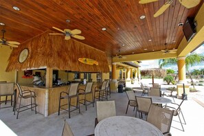 Un área de bar al aire libre con techo de madera y techumbre de paja, y varios arreglos de asientos.