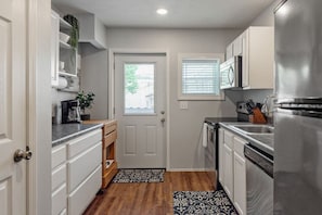 Cocina compacta con armarios blancos, un refrigerador de acero inoxidable y una ventana con persianas.