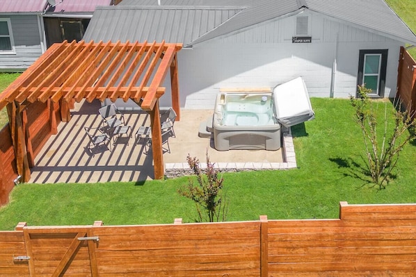 Un patio con un jacuzzi, una pérgola de madera y una pequeña zona de estar.