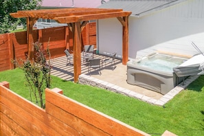 Een achtertuin met een houten pergola, een jacuzzi en een zithoek met stoelen en een tafel.
