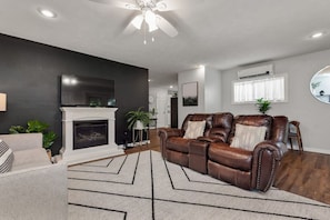 Una sala de estar con chimenea, sofá de cuero y ventilador de techo.