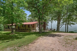 A lodge with a red roof, surrounded by trees, a gravel path, and a view of the mountains.