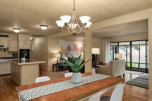A spacious kitchen with a central island, a dining area with a chandelier, and a view through large windows.