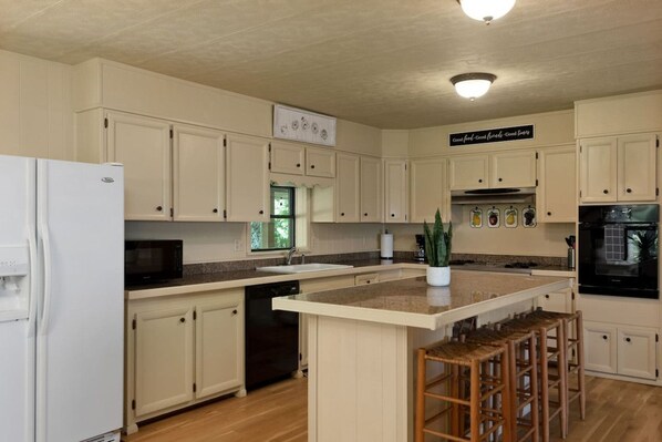 A kitchen with white cabinets, a central island with stools, a microwave, and a dishwasher.