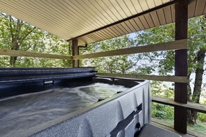 A hot tub under a wooden pergola with a view of trees.