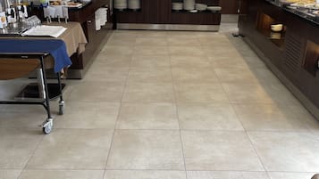 Zona de bufé con un chef preparando alimentos, una pantalla mostrando opciones de menú y mesas de bufé ordenadas con platos y cubiertos.