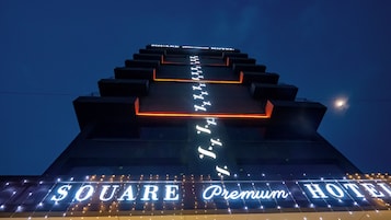 A hotel sign with the name "SQUARE Premium Hotel" illuminated in white letters against a dark sky.