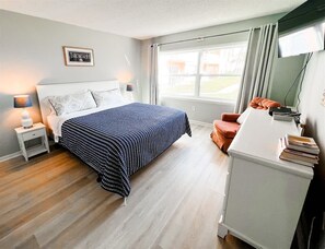 Ein Schlafzimmer mit Bett, Nachttisch, Lampe und Blick ins Freie.