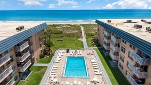 Un hôtel doté d’une piscine centrale entourée de chaises longues, offrant une vue sur la plage et comprenant plusieurs balcons.