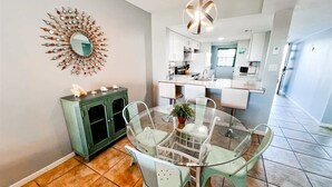 Un coin repas avec une table et des chaises en verre, un meuble vert et un miroir décoratif au mur.